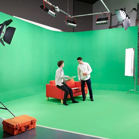 Two people on a sofa in front of the green screen